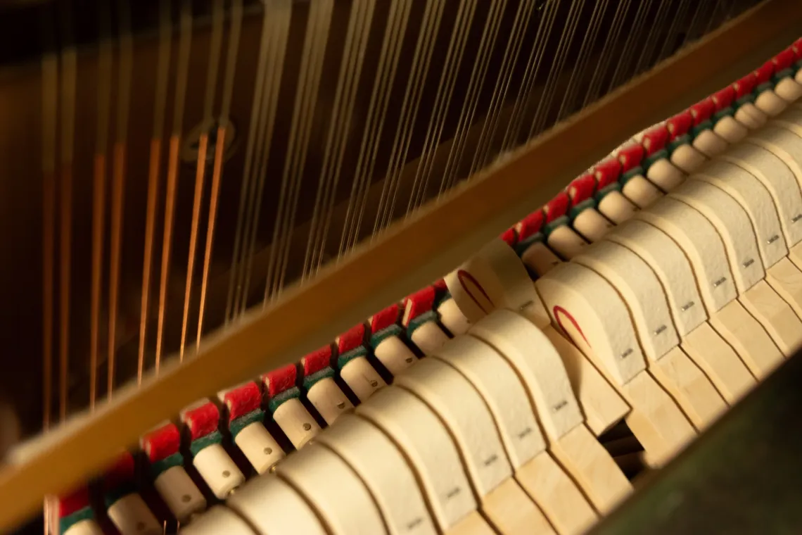 A row of hammers are lined up inside an upright piano, with one key pressed to strike the piano strings.
