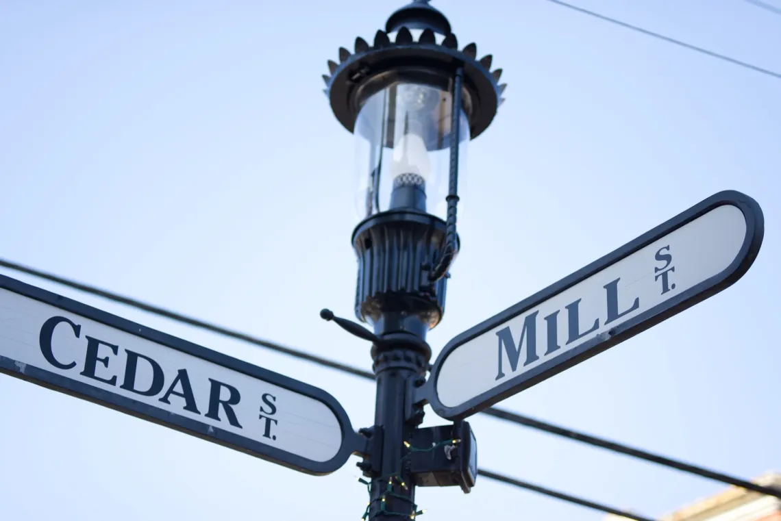 A black street lamp with road signs pointing to Cedar Street and Mill Street.