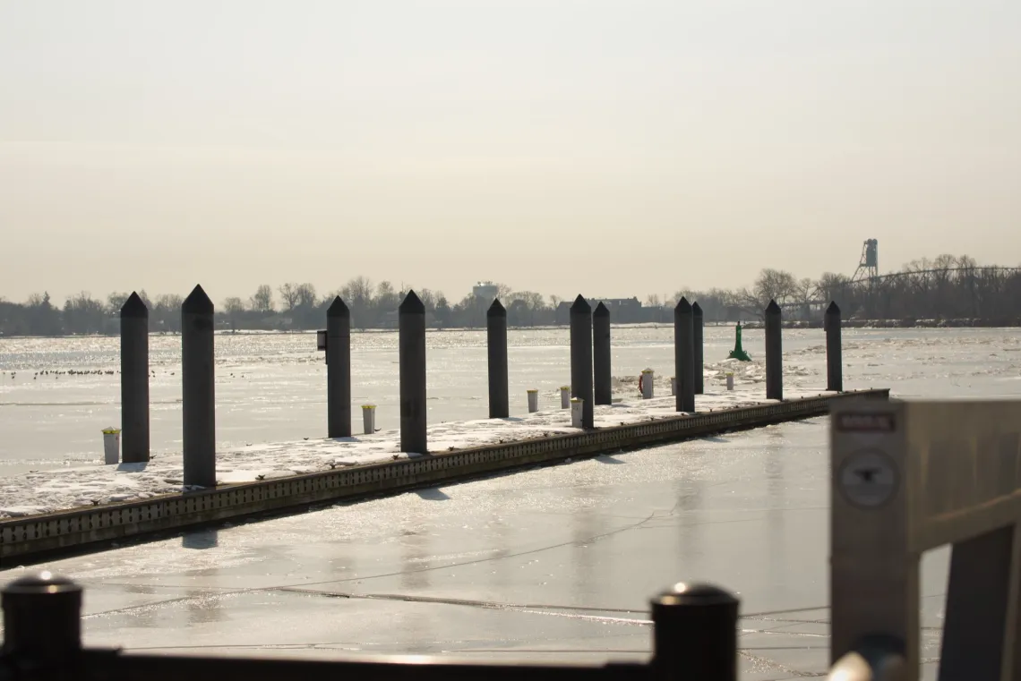 An empty wharf sits afloat on a river, with melting snow on top and melting ice below.