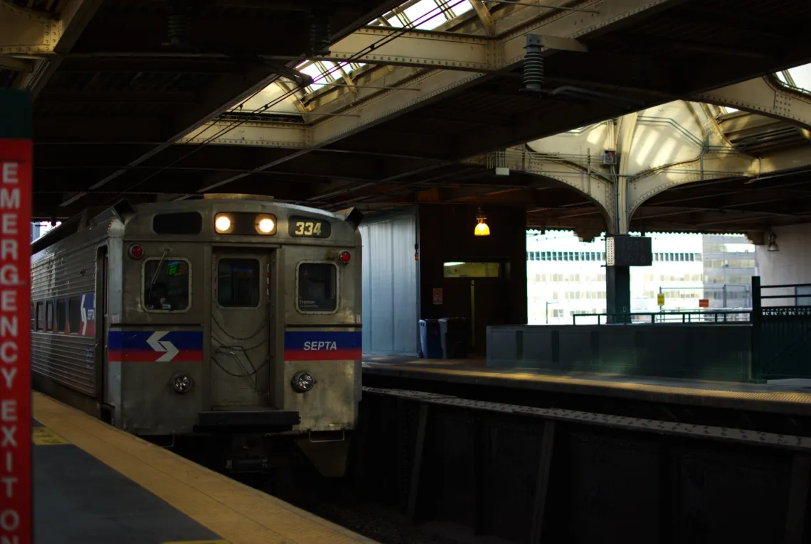 Passenger train approaches a dark train station platform. Golden sunset reflects on the metal beams overhead.