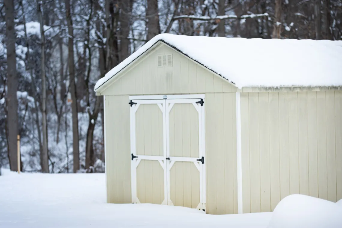 A lightly-colored wooden shed covered in snow. The doors are locked shut.
