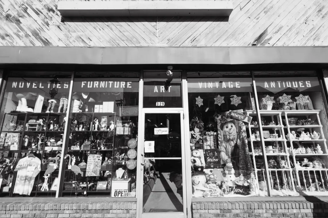 The entrance to an antique market, with many items propped up against big windows. The banner reads, "Novelties, Furniture, Art, Vintage, Antiques".