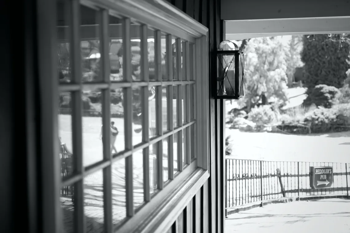 Along the wall, a reflective glass window is split into several panes by wooden bars. A historic-themed wall light is mounted next to the window.