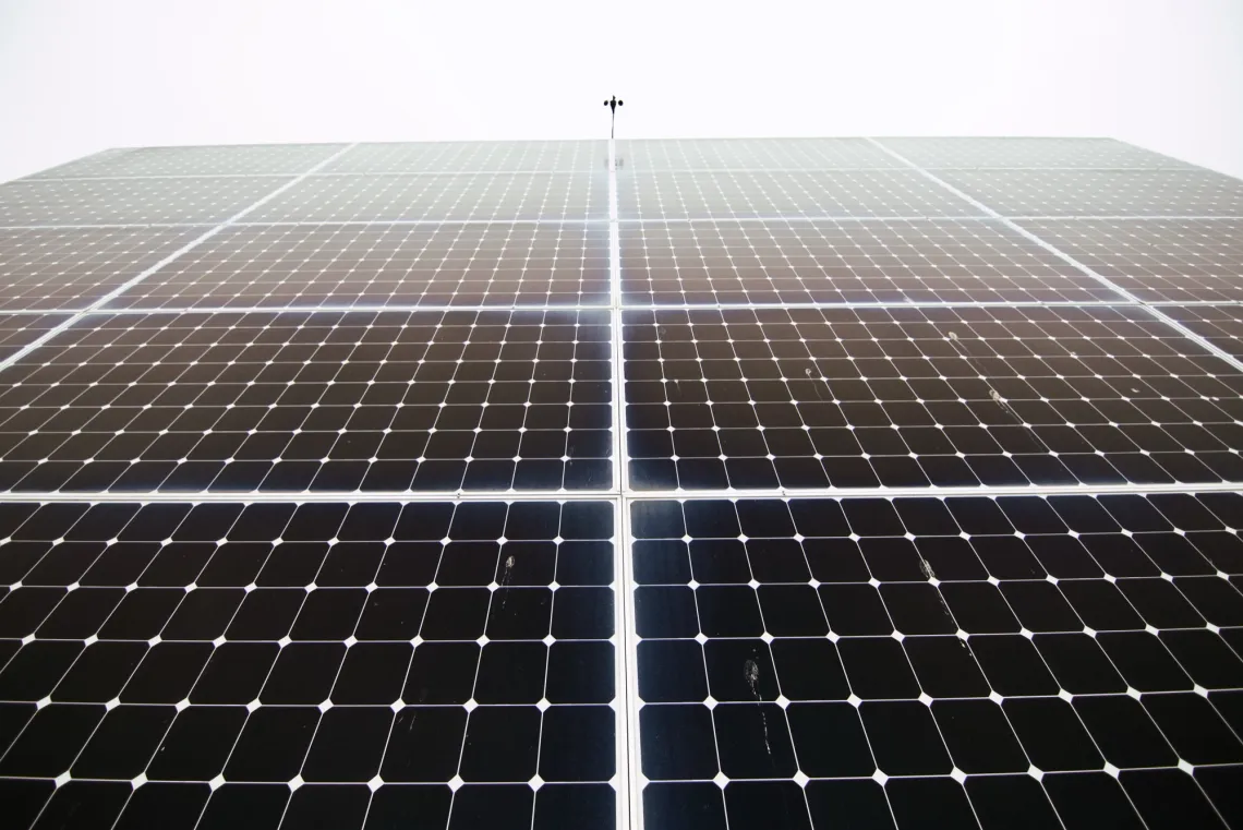 A wall of solar panels reflects the cloudy sky above.