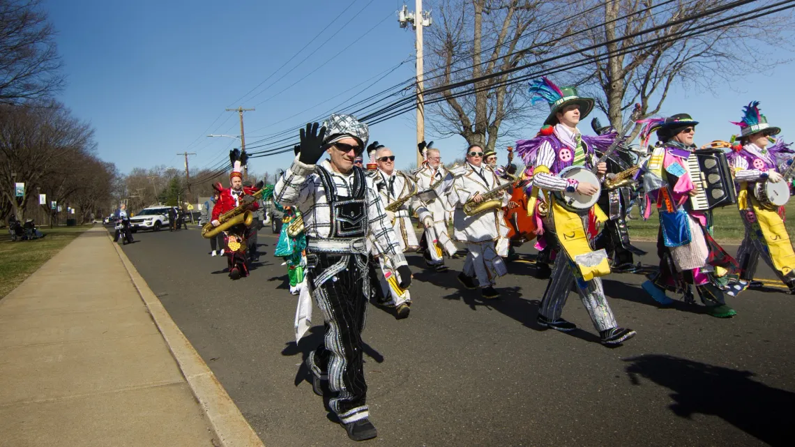 A man, dressed in sparkling attire for a St. Patrick's Day festival parade, waves to the camera.