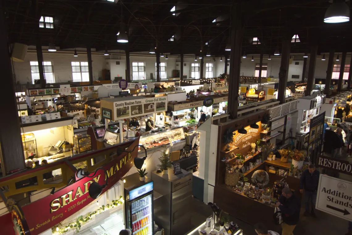 Rows of colorful booths in a market building selling flowers, meats, or other produce.