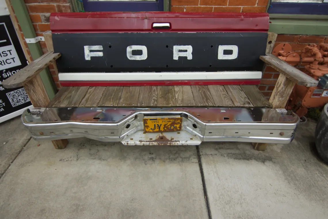 A wooden bench made from a vintage Ford truck tailgate sits on a sidewalk.