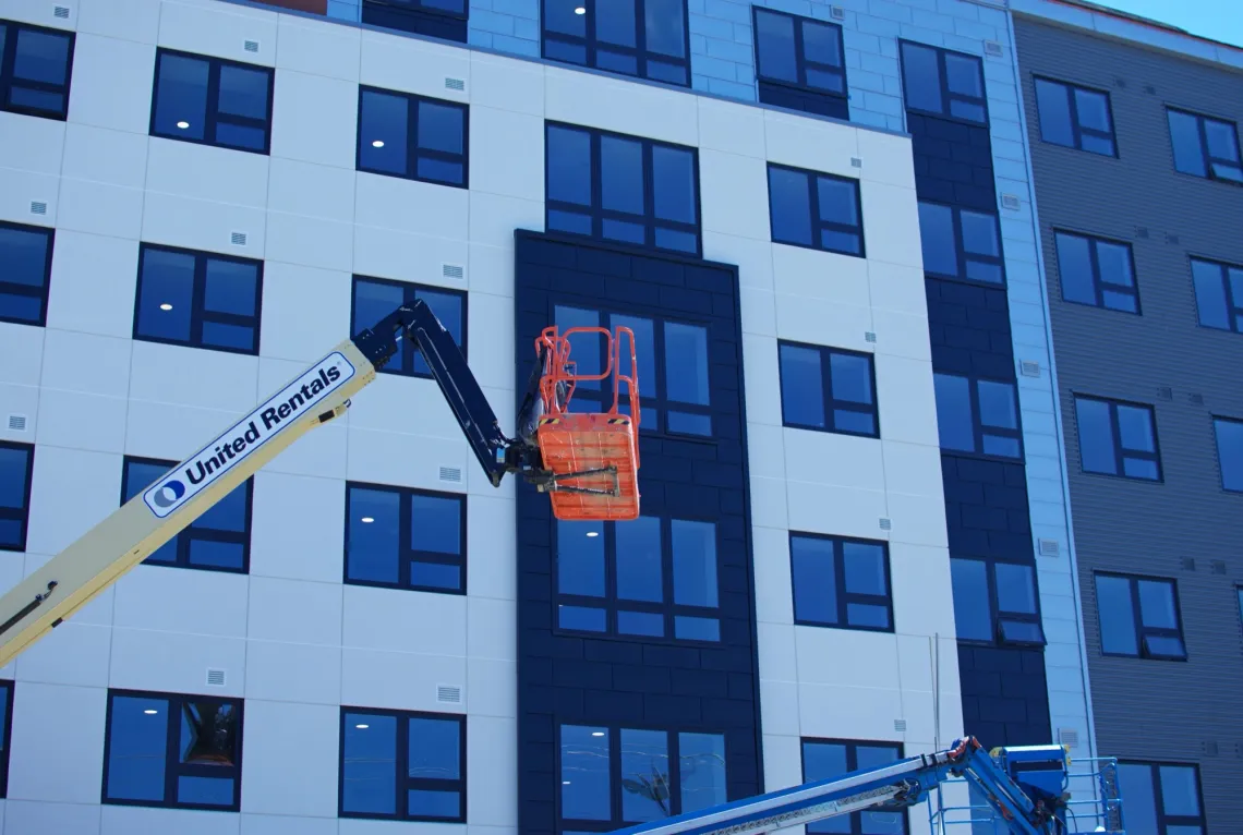 At a construction scene in front of a modern building, a yellow lifting work platform hovers in place.
