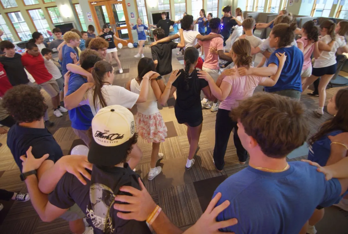 Students hold each other at the shoulder in circles facing inwards, dancing left and right.