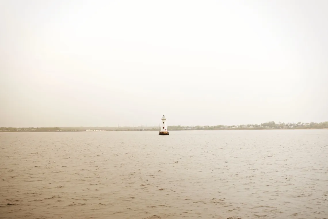 Stylized image of a distant lighthouse in the water, with the shore lining the horizon in the background.