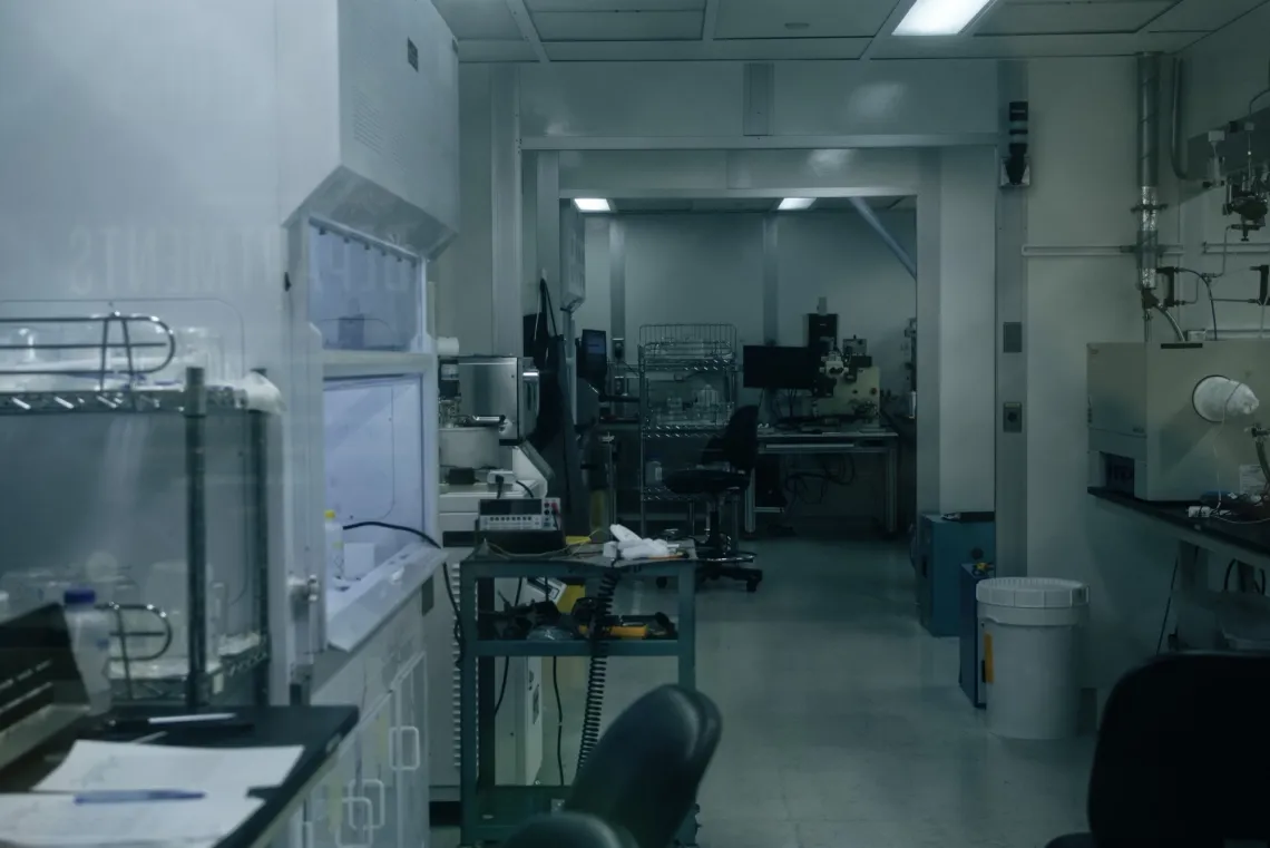An aisle of laboratory workspace, with a fume hood on the left and various scientific equipment down the hall.
