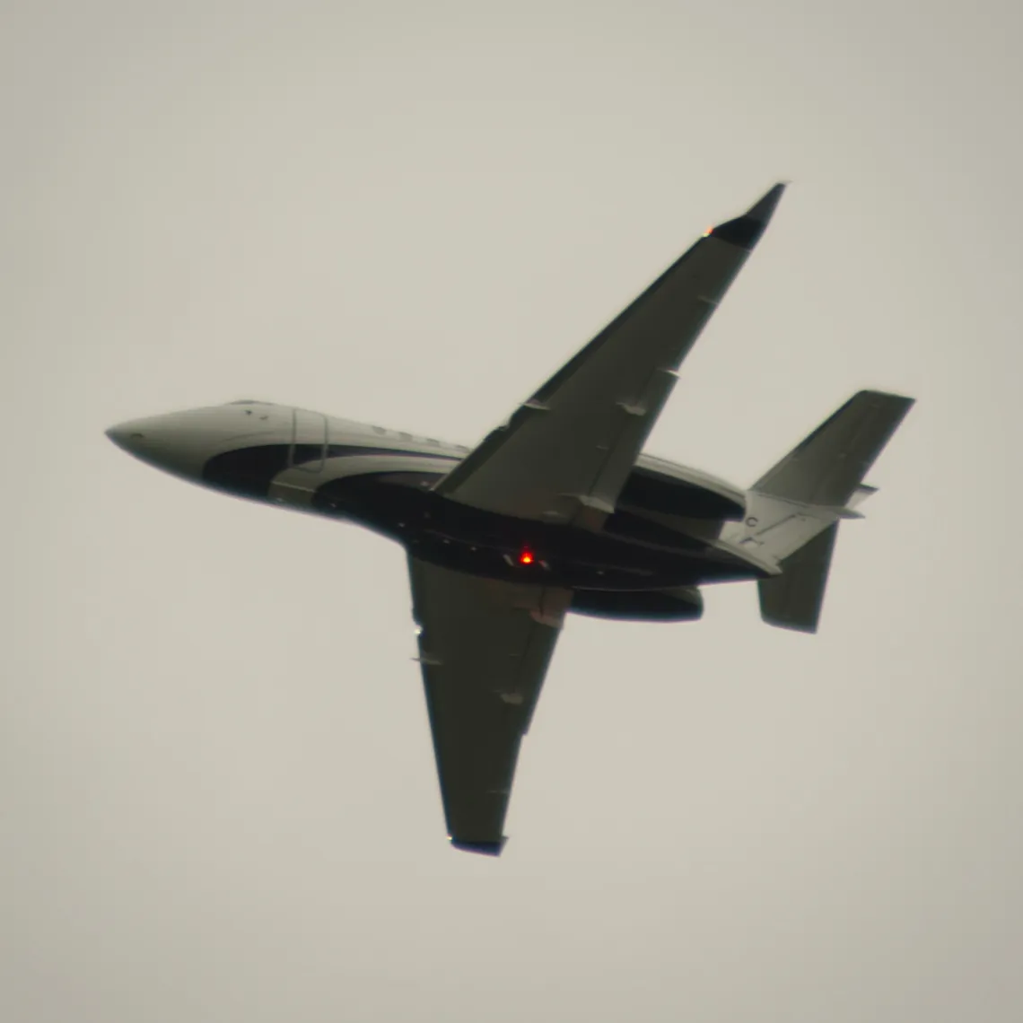 A small jet plane flies left in the gray sky.