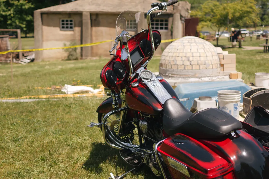 A red and black motorcycle with shiny gray accents is parked in front of brick sculptures on a grassy lawn.