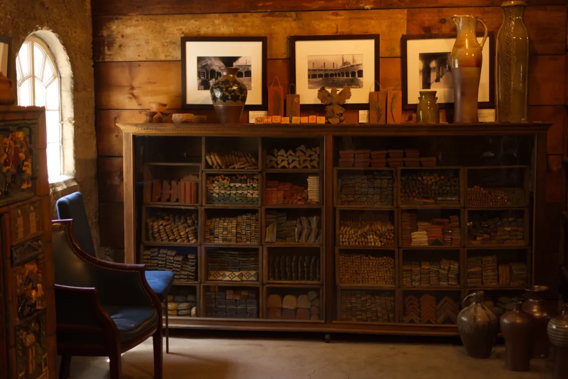 Sunlight through a window (left). A cabinet of various clay shapes is neatly sorted by shape. Paintings hang from the wall above the cabinet, while pots sit in front.