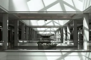 Open passageways in a mall run parallel, side-to-side. Sunlight from above reflects from windows and walls.