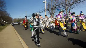 A man, dressed in sparkling attire for a St. Patrick's Day festival parade, waves to the camera.