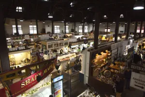 Rows of colorful booths in a market building selling flowers, meats, or other produce.