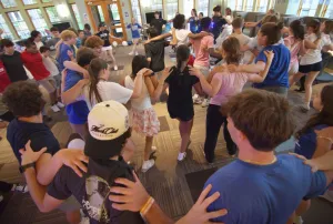 Students hold each other at the shoulder in circles facing inwards, dancing left and right.