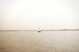 Stylized image of a distant lighthouse in the water, with the shore lining the horizon in the background.